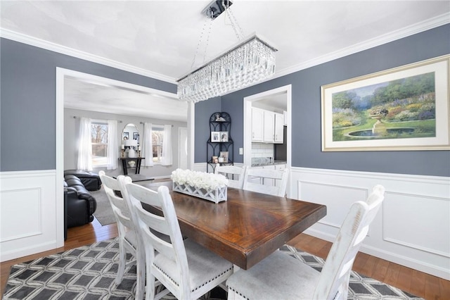 dining space featuring dark wood-style floors, ornamental molding, and wainscoting