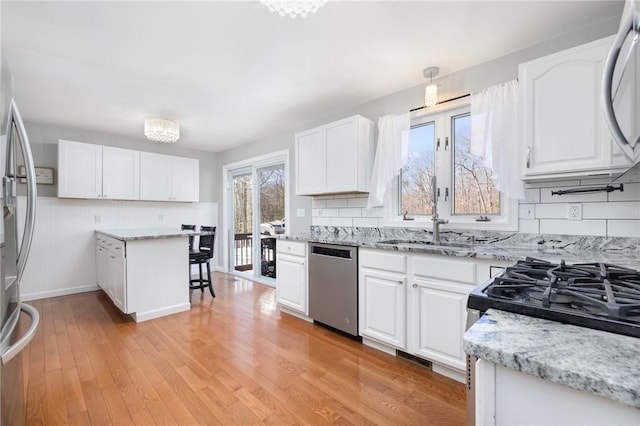 kitchen with appliances with stainless steel finishes, white cabinetry, light wood-style floors, and light stone counters