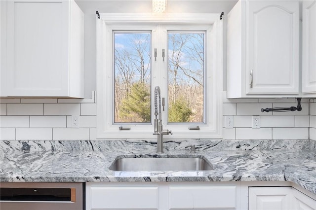 kitchen featuring dishwasher, a sink, white cabinets, and decorative backsplash