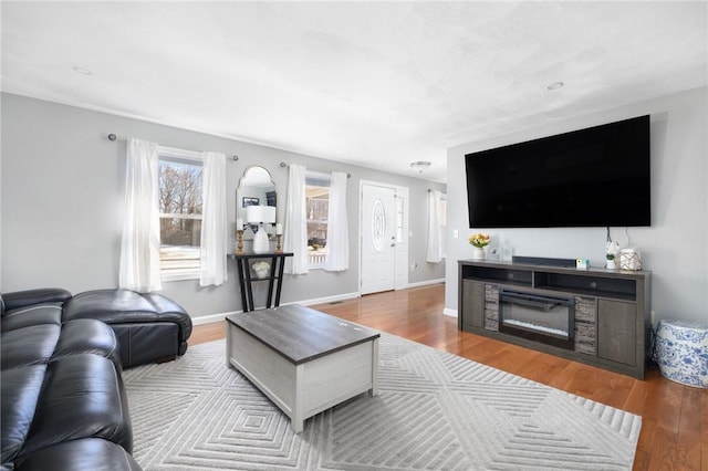 living area with a glass covered fireplace, wood finished floors, and baseboards