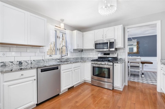 kitchen featuring a chandelier, light stone counters, appliances with stainless steel finishes, white cabinetry, and a sink