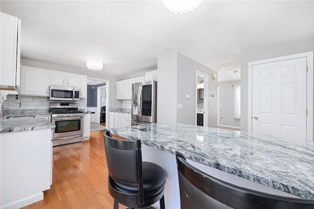 kitchen with appliances with stainless steel finishes, backsplash, white cabinets, and light wood-style flooring