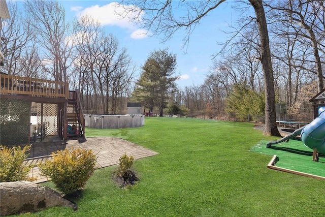 view of yard with a covered pool, stairs, a trampoline, a deck, and a patio area