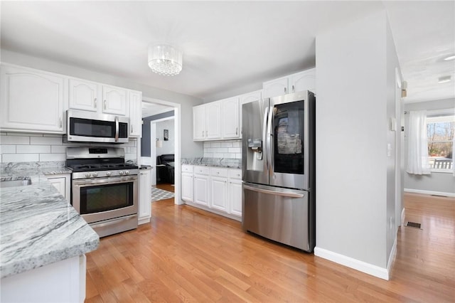 kitchen with light wood-style flooring, appliances with stainless steel finishes, light stone countertops, white cabinetry, and backsplash