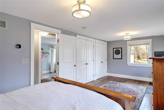 bedroom featuring dark wood-style floors, visible vents, baseboards, and two closets