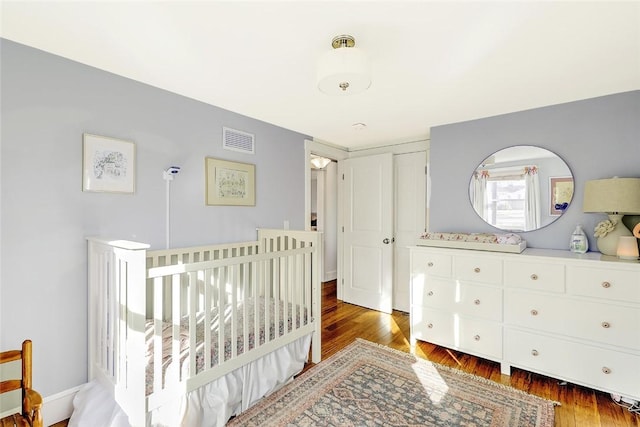 bedroom with a nursery area, visible vents, and wood finished floors