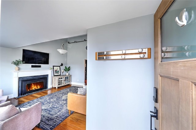 living room featuring lofted ceiling, a warm lit fireplace, and wood finished floors