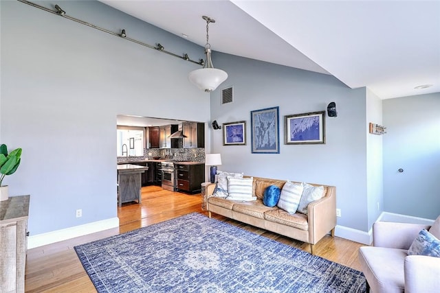 living area with high vaulted ceiling, light wood-type flooring, visible vents, and baseboards