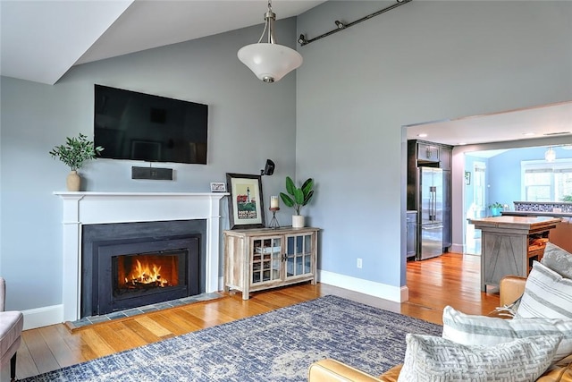 living room featuring lofted ceiling, a lit fireplace, wood finished floors, and baseboards