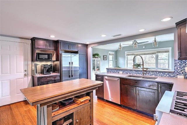 kitchen featuring visible vents, a sink, stainless steel appliances, light wood-style floors, and backsplash