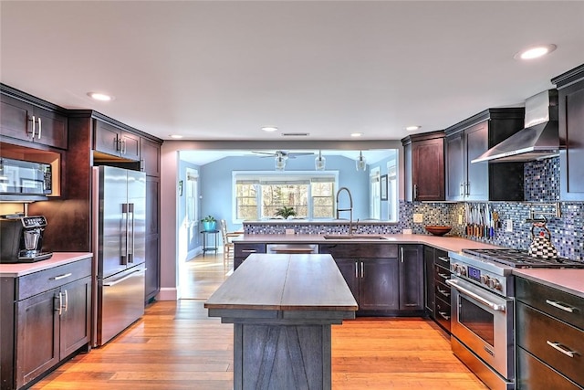 kitchen featuring premium appliances, tasteful backsplash, a sink, a peninsula, and wall chimney exhaust hood