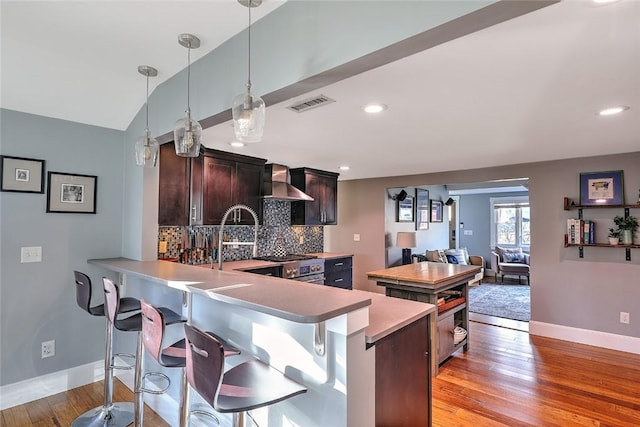 kitchen featuring light wood-style flooring, visible vents, light countertops, backsplash, and wall chimney exhaust hood