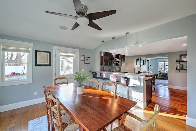 dining space with vaulted ceiling, ceiling fan, light wood-type flooring, and baseboards