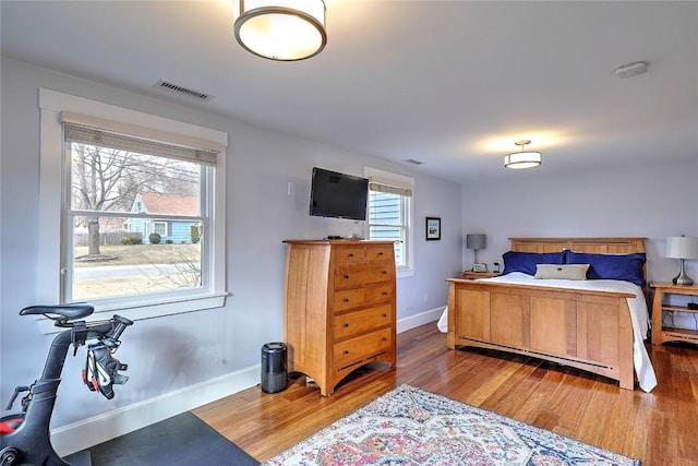 bedroom with multiple windows, wood finished floors, visible vents, and baseboards