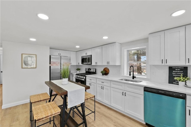 kitchen with a sink, stainless steel appliances, light countertops, and white cabinets