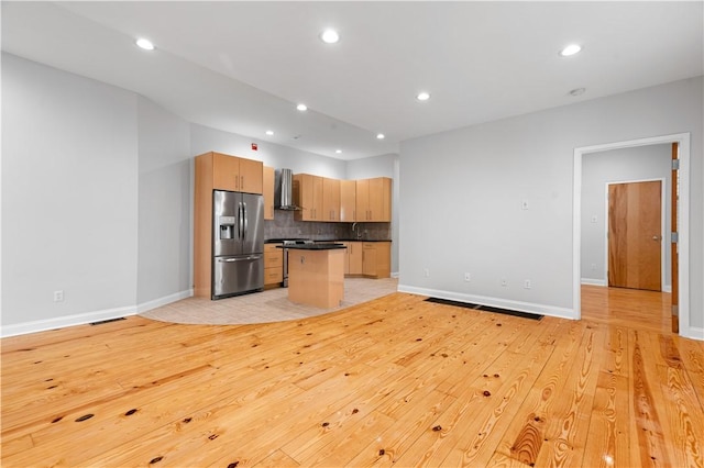 kitchen featuring dark countertops, appliances with stainless steel finishes, open floor plan, a kitchen island, and wall chimney exhaust hood