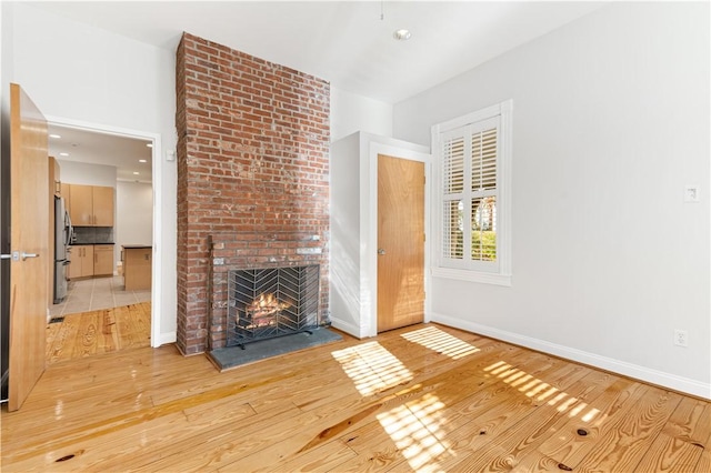 unfurnished living room with light wood finished floors, a brick fireplace, and baseboards