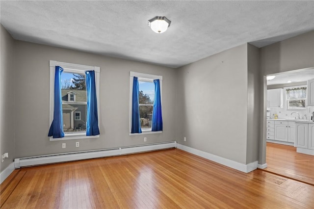 empty room with light wood-type flooring, a baseboard radiator, and a healthy amount of sunlight