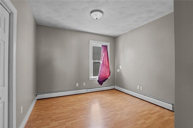 empty room with light wood finished floors, baseboard heating, and baseboards