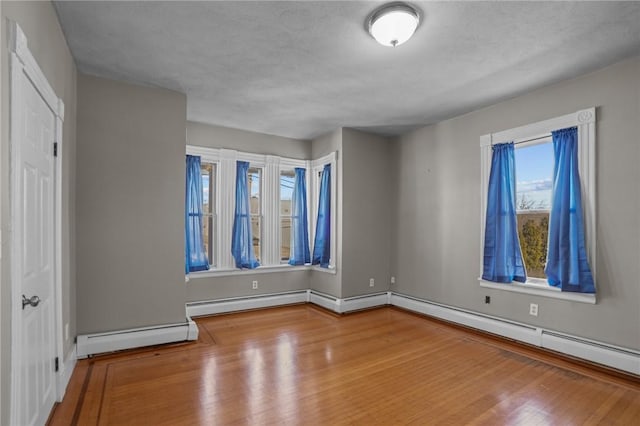 unfurnished bedroom with a textured ceiling, baseboard heating, wood finished floors, and baseboards