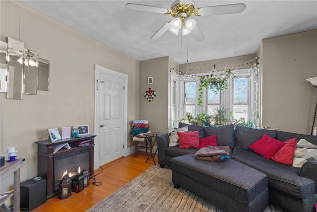 living area featuring a glass covered fireplace, wood finished floors, and a ceiling fan