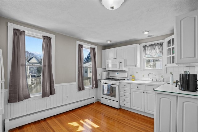 kitchen featuring a baseboard heating unit, white appliances, light countertops, and white cabinetry