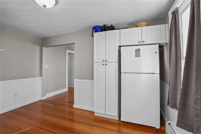 kitchen with light wood-style flooring, a wainscoted wall, white cabinets, baseboard heating, and freestanding refrigerator