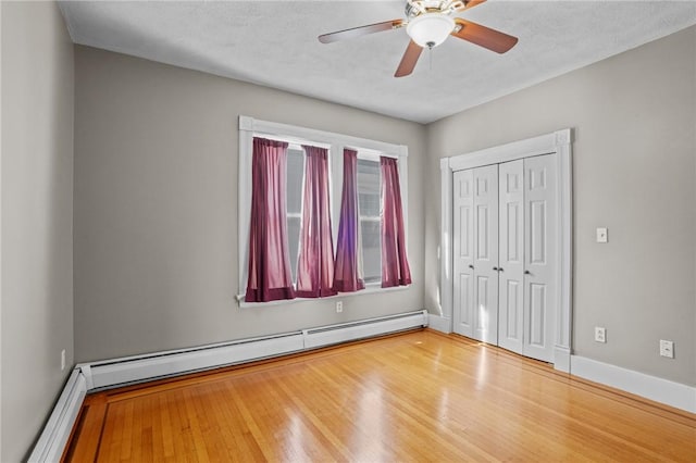 unfurnished bedroom featuring baseboards, ceiling fan, wood finished floors, baseboard heating, and a closet