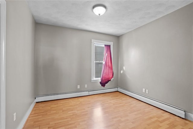 spare room with a baseboard radiator, baseboards, and light wood finished floors