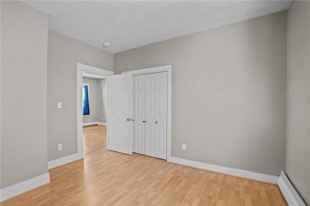 unfurnished bedroom with a baseboard radiator, baseboards, and light wood finished floors