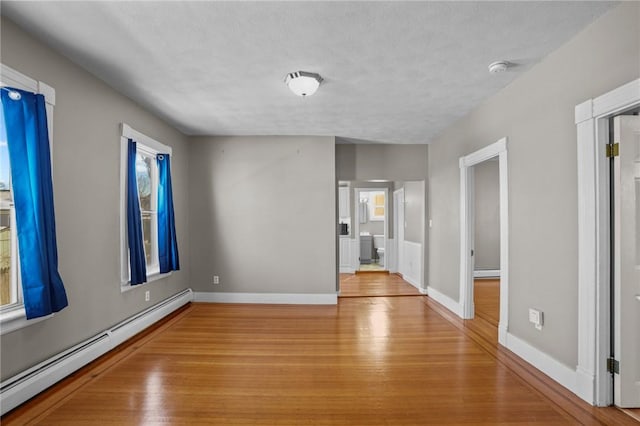 unfurnished room featuring a textured ceiling, light wood finished floors, baseboard heating, and baseboards