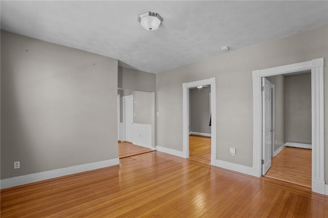 empty room with light wood-type flooring, baseboards, and a baseboard heating unit