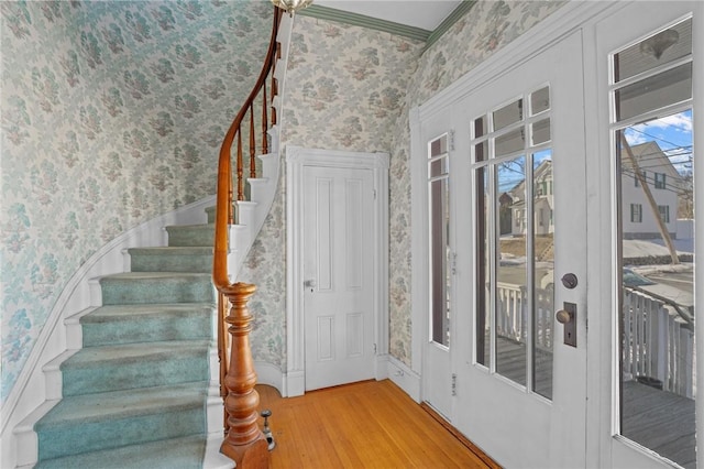 entrance foyer featuring stairs, wood finished floors, crown molding, and wallpapered walls