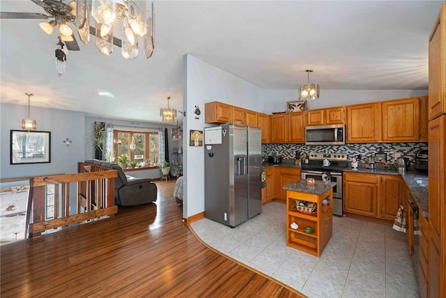 kitchen featuring decorative backsplash, appliances with stainless steel finishes, brown cabinetry, open floor plan, and a kitchen island