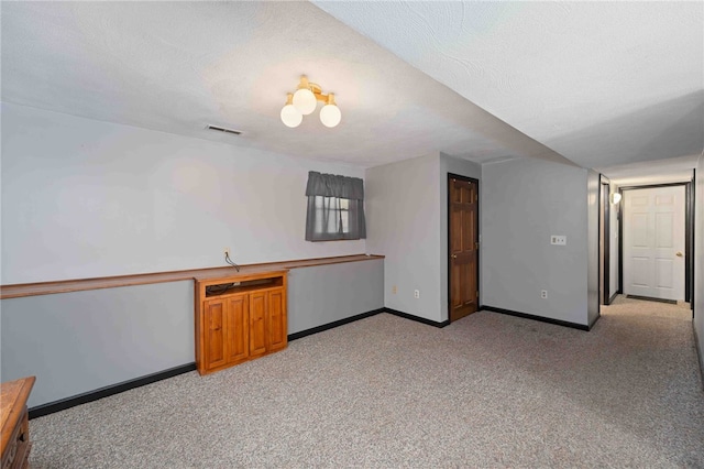 interior space featuring a textured ceiling, baseboards, visible vents, and light colored carpet