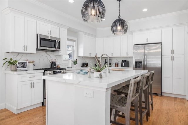 kitchen featuring pendant lighting, a center island with sink, crown molding, stainless steel appliances, and white cabinets