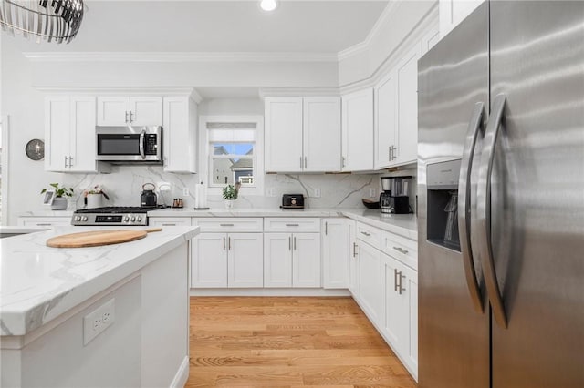 kitchen with appliances with stainless steel finishes, light wood-style floors, ornamental molding, white cabinets, and light stone countertops