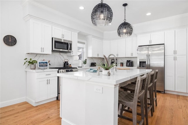 kitchen with appliances with stainless steel finishes, white cabinets, decorative light fixtures, and an island with sink