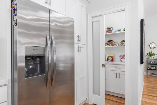 kitchen with light countertops, light wood-style flooring, stainless steel refrigerator with ice dispenser, and white cabinetry