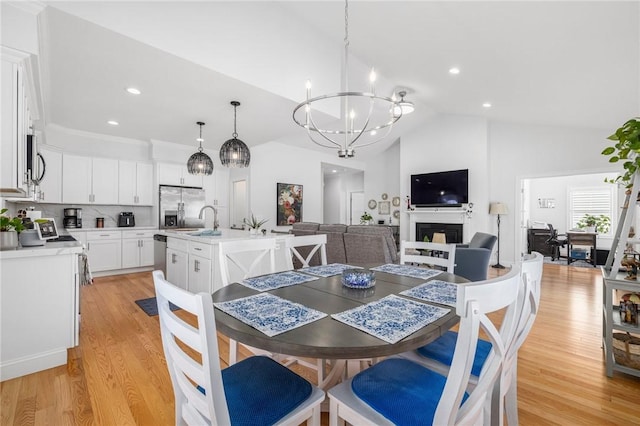 dining room featuring lofted ceiling, light wood-style floors, a fireplace, a chandelier, and recessed lighting