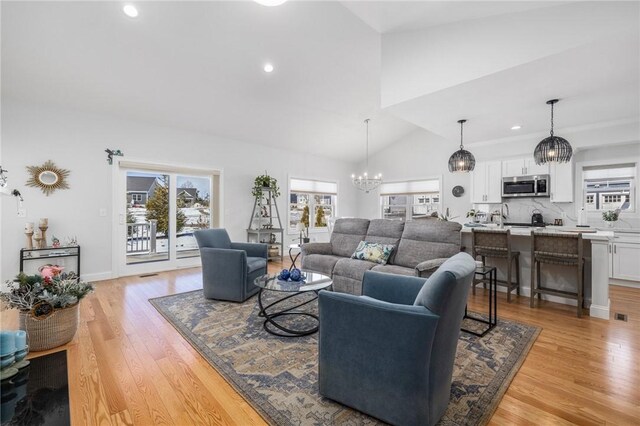 living area with high vaulted ceiling, recessed lighting, light wood finished floors, and an inviting chandelier