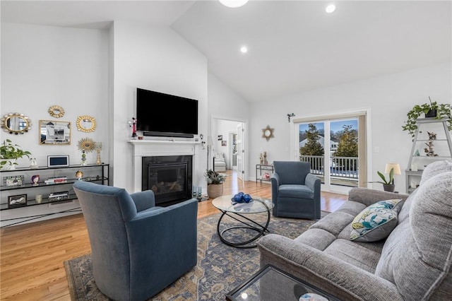 living room with recessed lighting, high vaulted ceiling, wood finished floors, and a glass covered fireplace