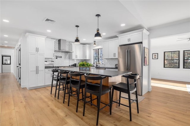 kitchen with light wood finished floors, white cabinets, dark countertops, freestanding refrigerator, and wall chimney range hood