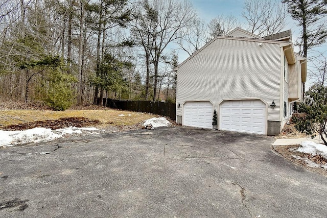 view of home's exterior featuring a garage, aphalt driveway, and fence