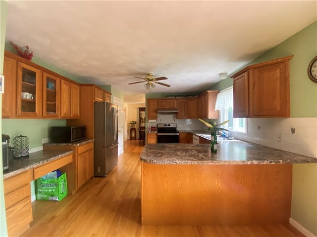 kitchen with stainless steel appliances, brown cabinetry, glass insert cabinets, a peninsula, and under cabinet range hood