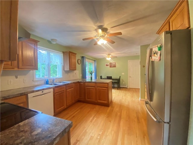 kitchen featuring dark countertops, freestanding refrigerator, white dishwasher, a sink, and a peninsula