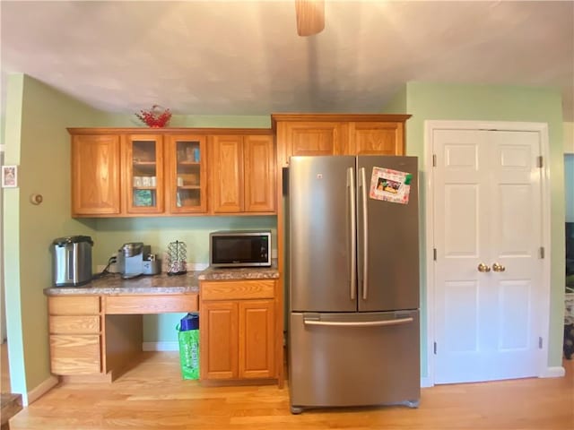 kitchen featuring brown cabinetry, glass insert cabinets, light stone countertops, stainless steel appliances, and light wood-type flooring