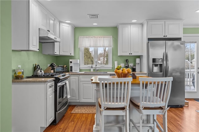 kitchen with stainless steel appliances, visible vents, white cabinets, a sink, and under cabinet range hood