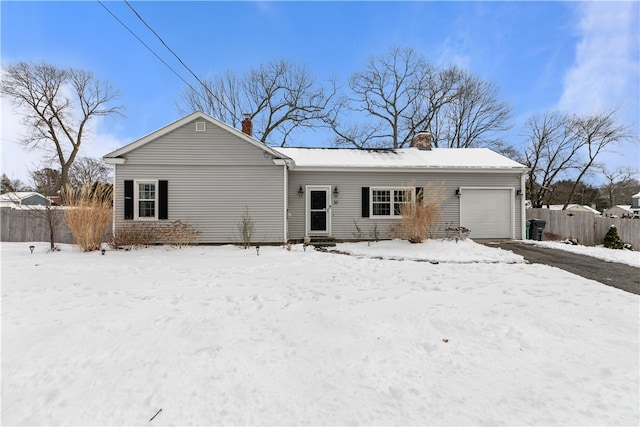 snow covered back of property with fence, a chimney, and an attached garage