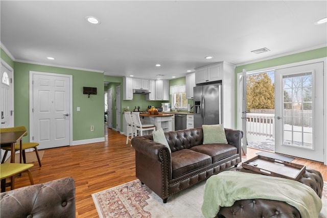 living area featuring recessed lighting, visible vents, baseboards, ornamental molding, and light wood finished floors